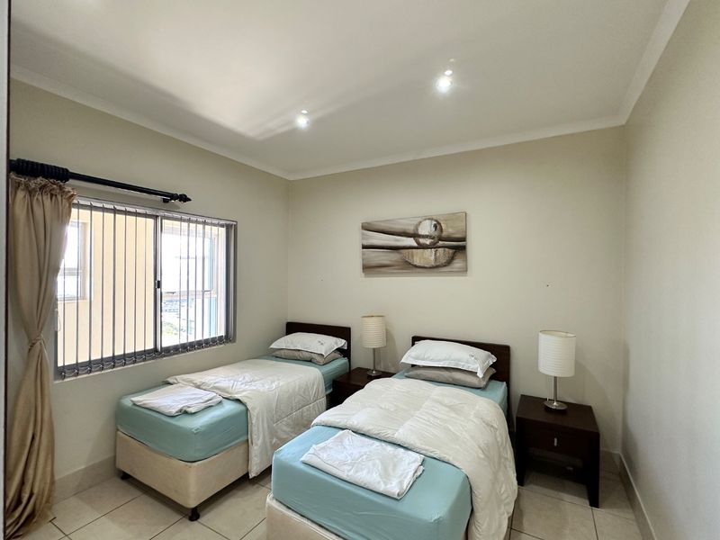 A well-maintained bedroom featuring neutral wall tones, tiled flooring, and a sliding window with integrated curtain hardware.