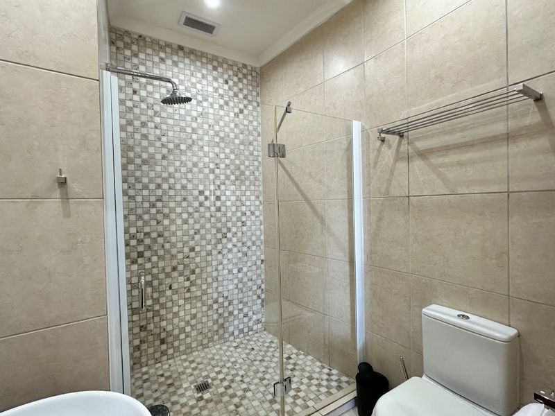 A modern bathroom featuring a walk-in shower with a rainfall shower head, mosaic tile accents, and neutral ceramic wall and floor tiles.