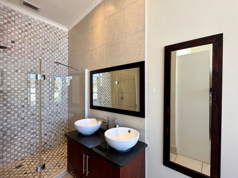 Modern bathroom featuring a double vanity with vessel sinks, granite countertop, and a spacious walk-in shower with decorative mosaic tiling.