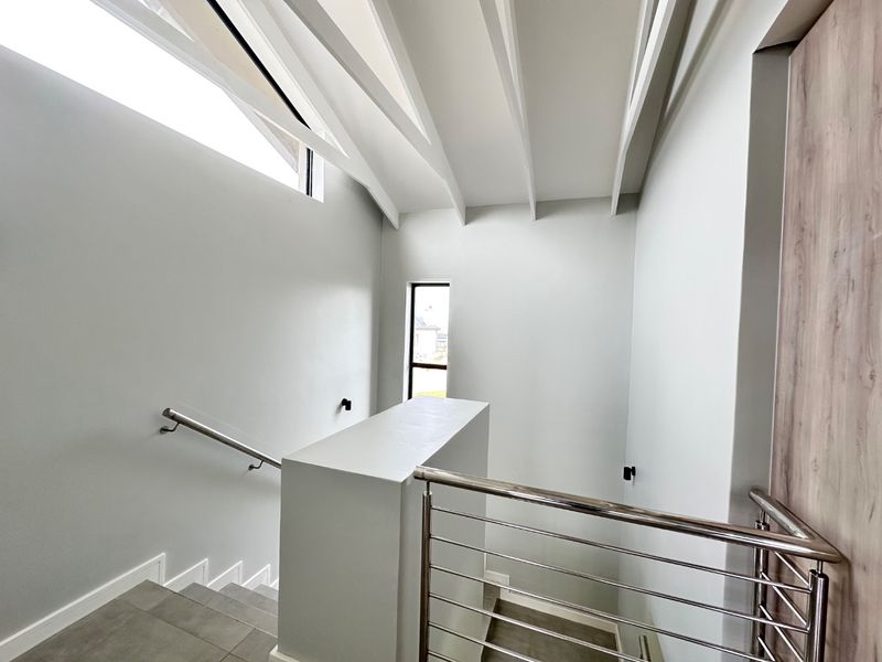 Modern staircase area featuring exposed ceiling beams, a skylight for natural light, and a sleek stainless steel balustrade with tiled flooring.