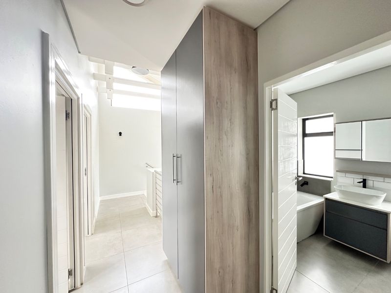 A bright, modern hallway featuring neutral tiled flooring, built-in storage cabinetry, and direct access to an adjacent bathroom.