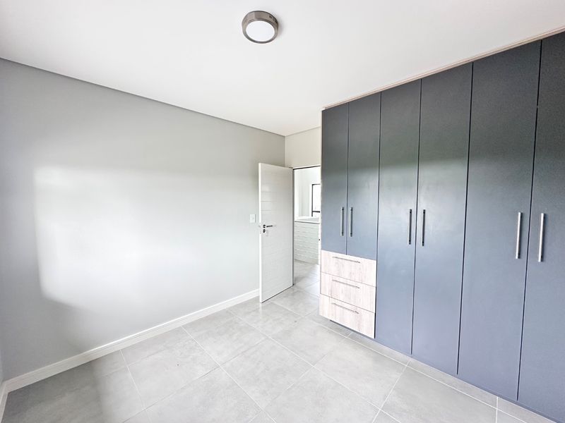 A bright, modern bedroom featuring neutral grey tiled flooring, a minimalist ceiling light, and extensive built-in cabinetry with a contemporary two-tone finish.