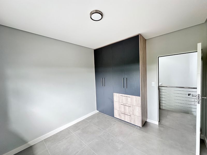 A modern, empty bedroom featuring neutral grey tiled flooring, built-in cupboards with a two-tone finish, and a clean, minimalist aesthetic.
