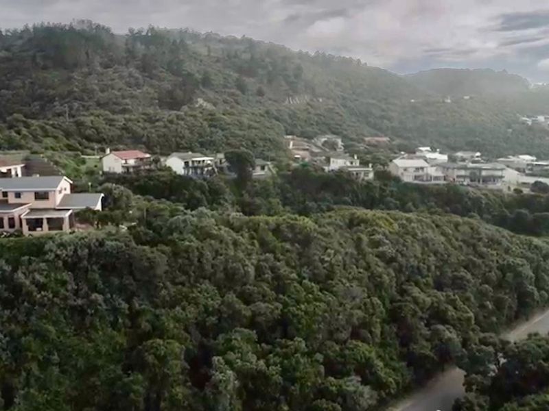 An aerial view of a residential area nestled within a hilly, densely vegetated landscape.