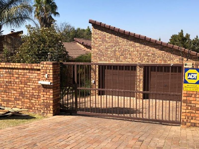 Front view of a face brick house featuring a double garage, paved driveway, and secure perimeter fencing with an automated sliding gate.