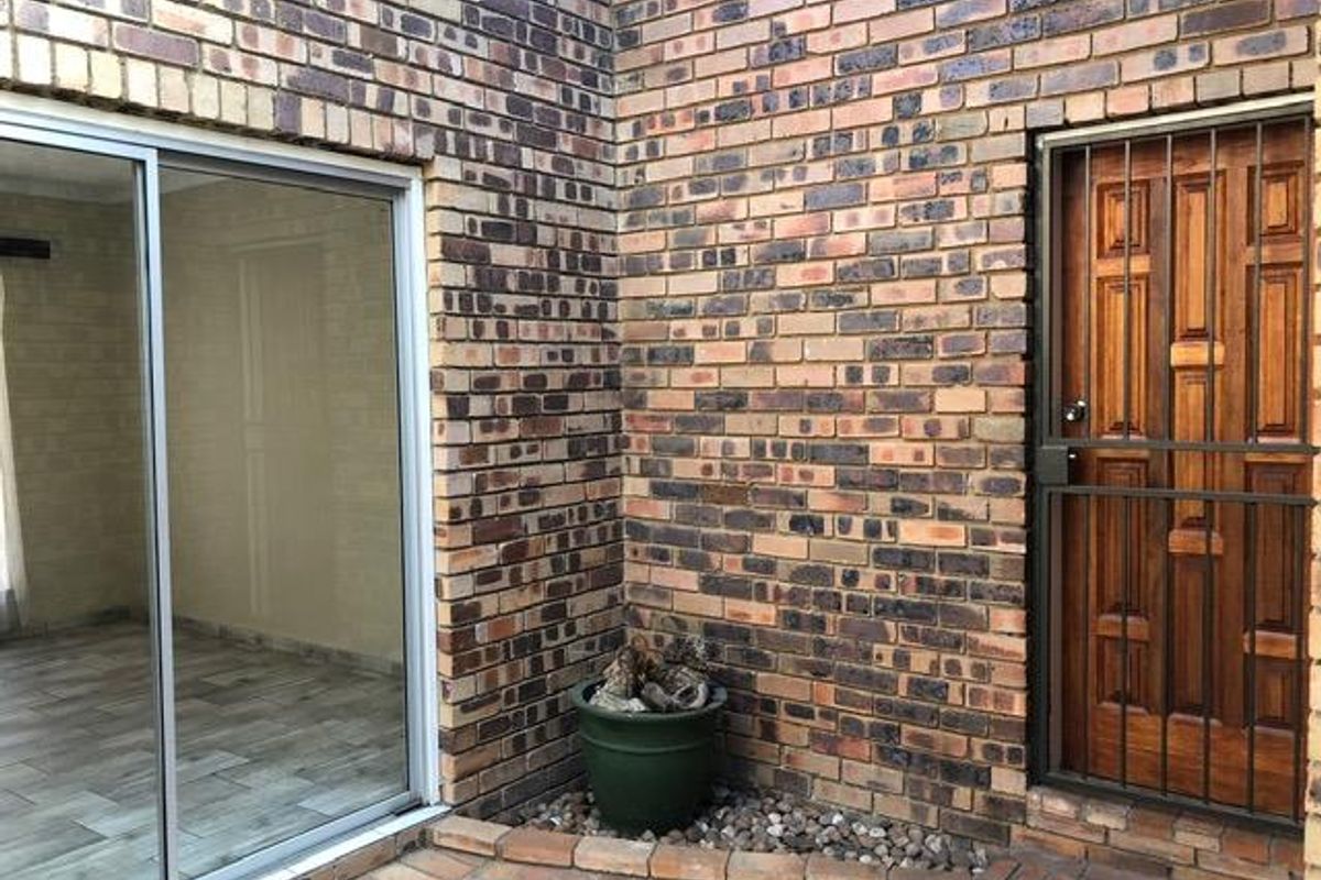 A rear exterior view featuring face brick walls, a sliding glass door, and a timber door with a security gate.