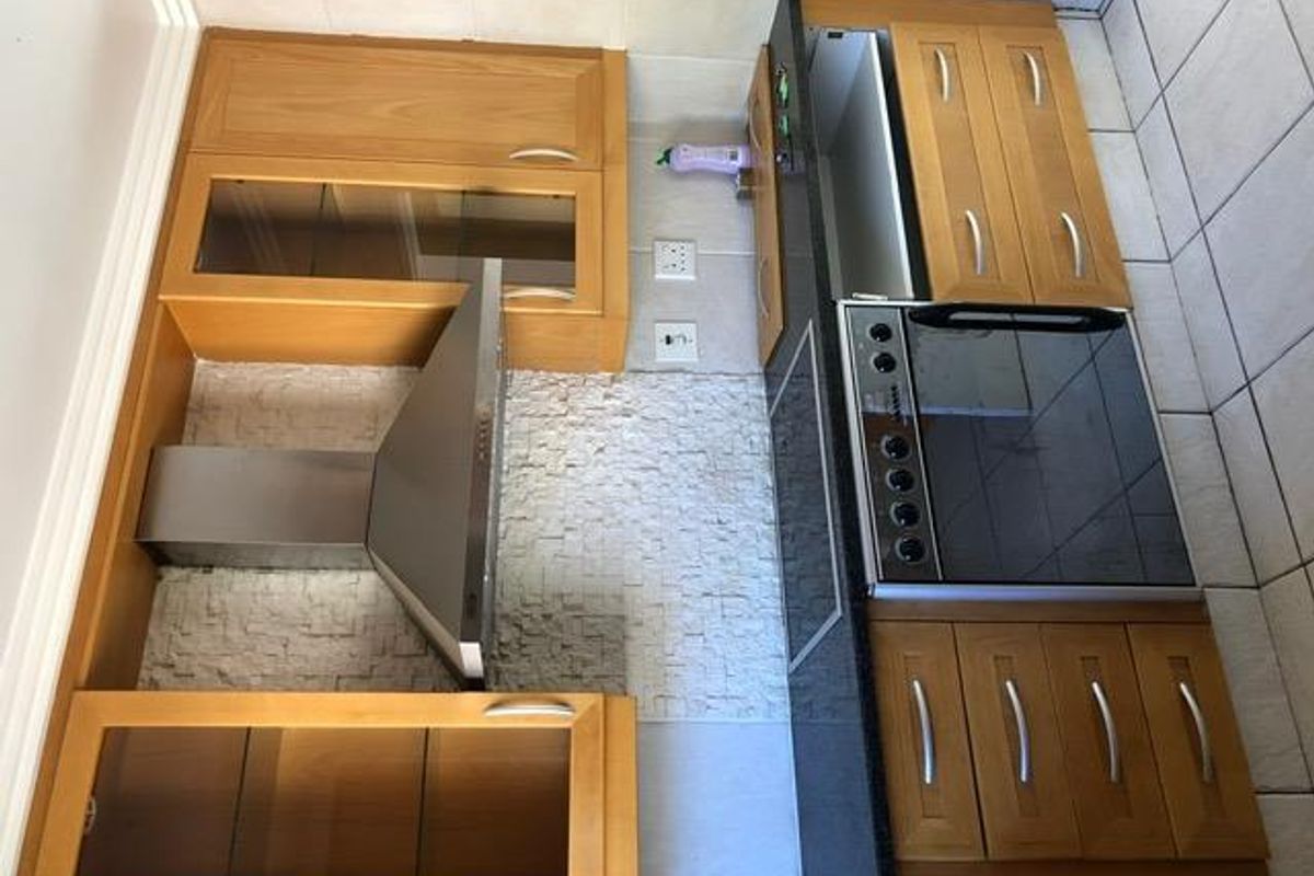 A functional kitchen featuring wooden cabinetry, granite countertops, a stone backsplash, and integrated stainless steel appliances, including an oven and extractor fan.