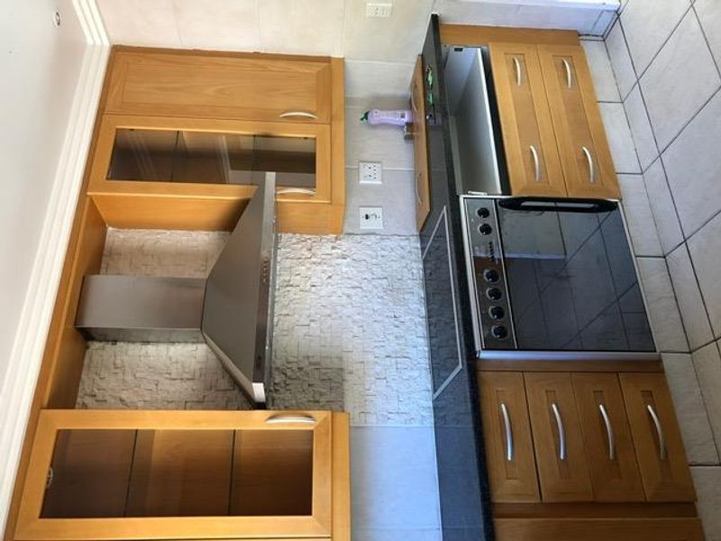 A functional kitchen featuring wooden cabinetry, granite countertops, a stone backsplash, and integrated stainless steel appliances, including an oven and extractor fan.