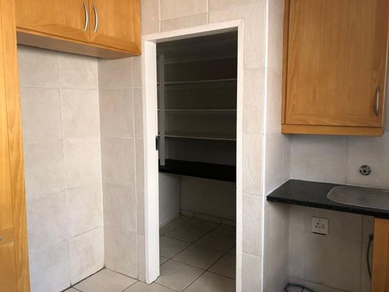 A functional scullery area featuring built-in wooden cabinetry, tiled finishes, a sink, and a separate walk-in pantry space with fixed shelving.