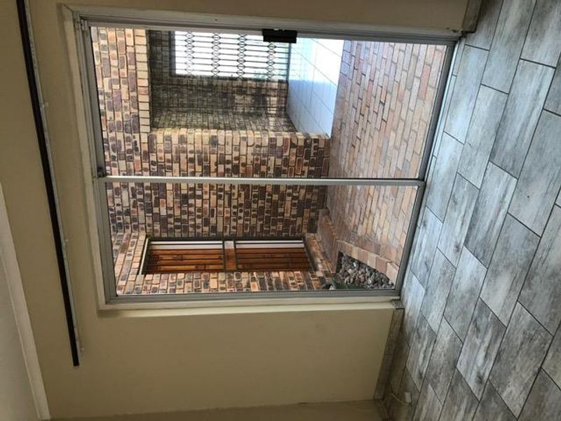 A view from an interior room looking out onto a private brick-paved courtyard with security gates and exposed brick walls.