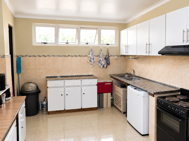 Functional kitchen featuring granite countertops, white cabinetry, double basin sink, and built-in electric stove with extractor fan, finished with tiled backsplash and flooring.