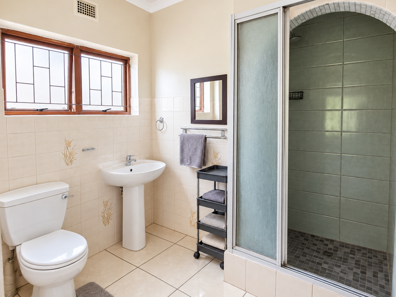 A functional bathroom featuring a pedestal basin, toilet, and a separate shower enclosure with tiled finishes and a window for natural light.