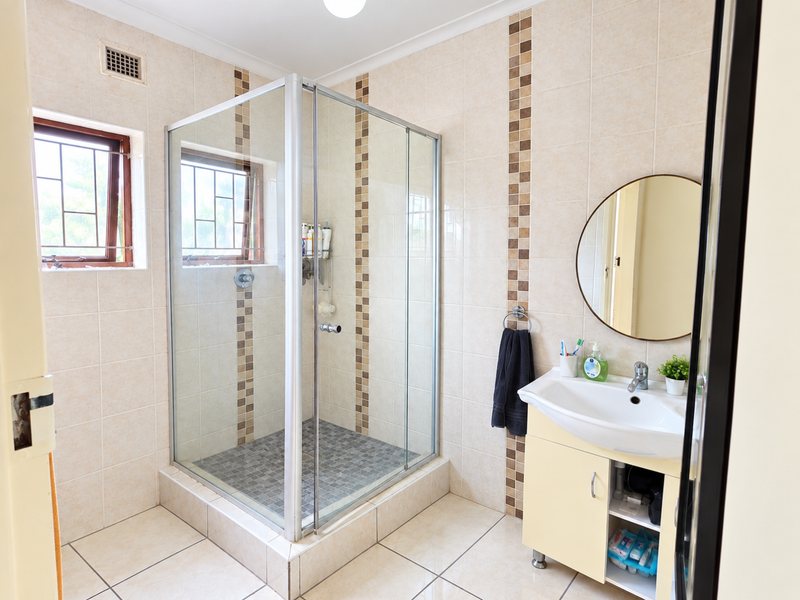 A functional bathroom featuring a glass-enclosed shower, a vanity unit with a basin, and neutral wall tiling with decorative mosaic accents.