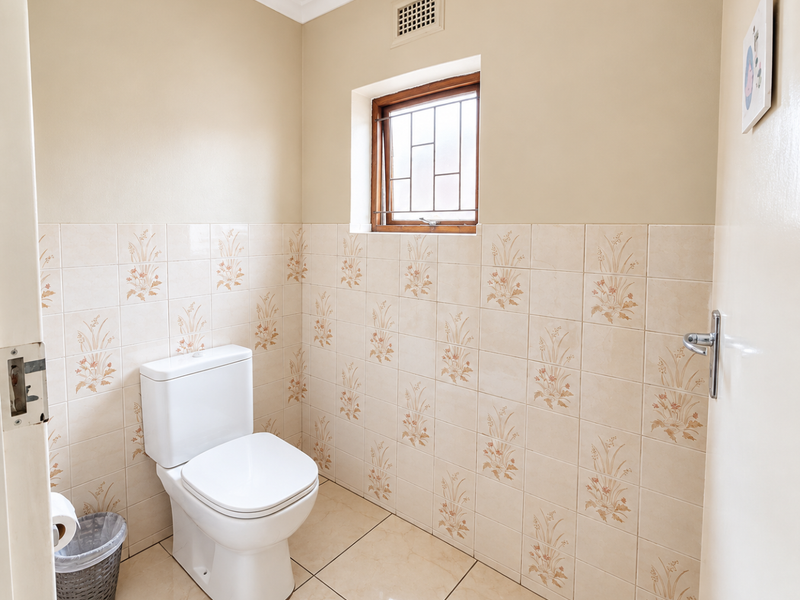 A functional bathroom featuring tiled walls and flooring, a standard toilet, and a window with security bars for ventilation.
