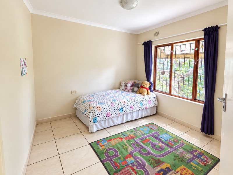 A bright bedroom featuring tiled flooring, wooden window frames with security bars, and neutral wall finishes.