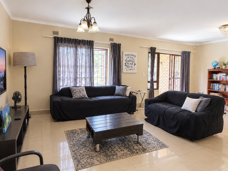 Spacious living room featuring neutral tiled flooring, large windows with security bars, and direct access to an outdoor area through a sliding glass door.