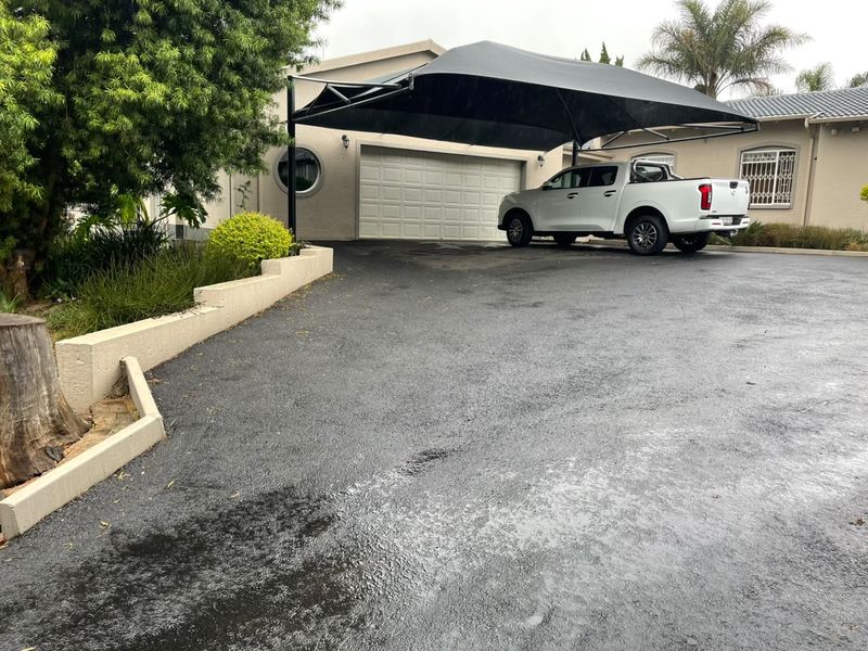 Front exterior view featuring a paved driveway, a garage with a sectional door, and a modern shade sail structure for vehicle protection.