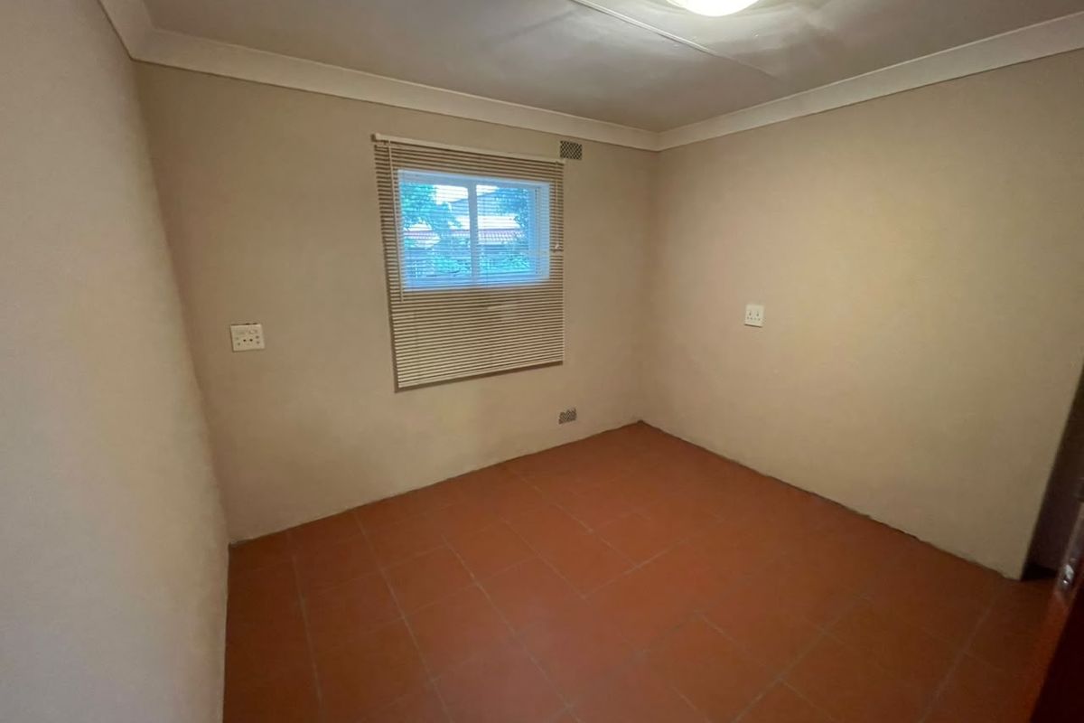An empty bedroom featuring neutral wall paint, tiled flooring, and a fitted window blind, providing a blank canvas for personalization.