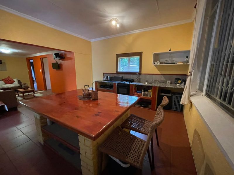 A dated kitchen featuring a large built-in island, basic cabinetry, and tiled flooring, opening into an adjacent living area.