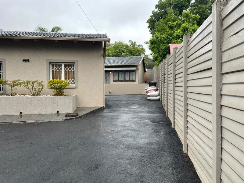 A view of the property driveway featuring a paved surface, precast concrete boundary wall, and exterior building facade with security window bars.