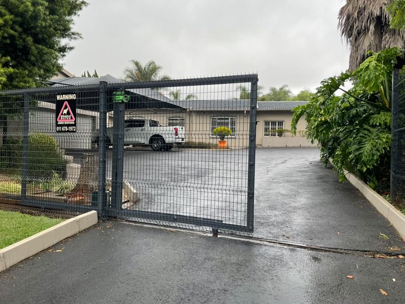 Front view of the property featuring a secure gated entrance, paved driveway, and a carport providing covered parking.
