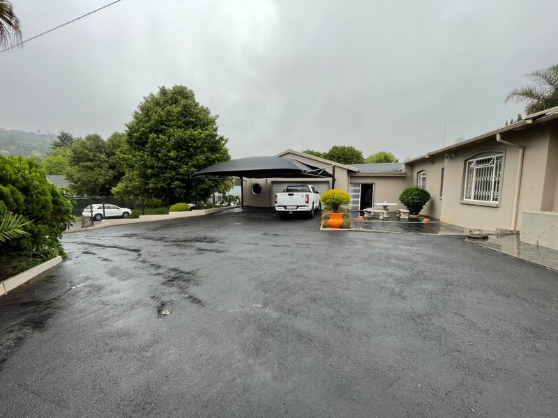 Front exterior view featuring a spacious asphalt driveway, a shade sail carport, and a single garage entrance.