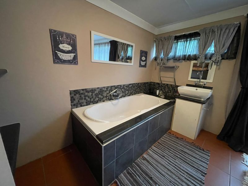 A functional bathroom featuring a built-in bathtub with dark tile surround, a modern vessel sink on a vanity cabinet, and tiled flooring.
