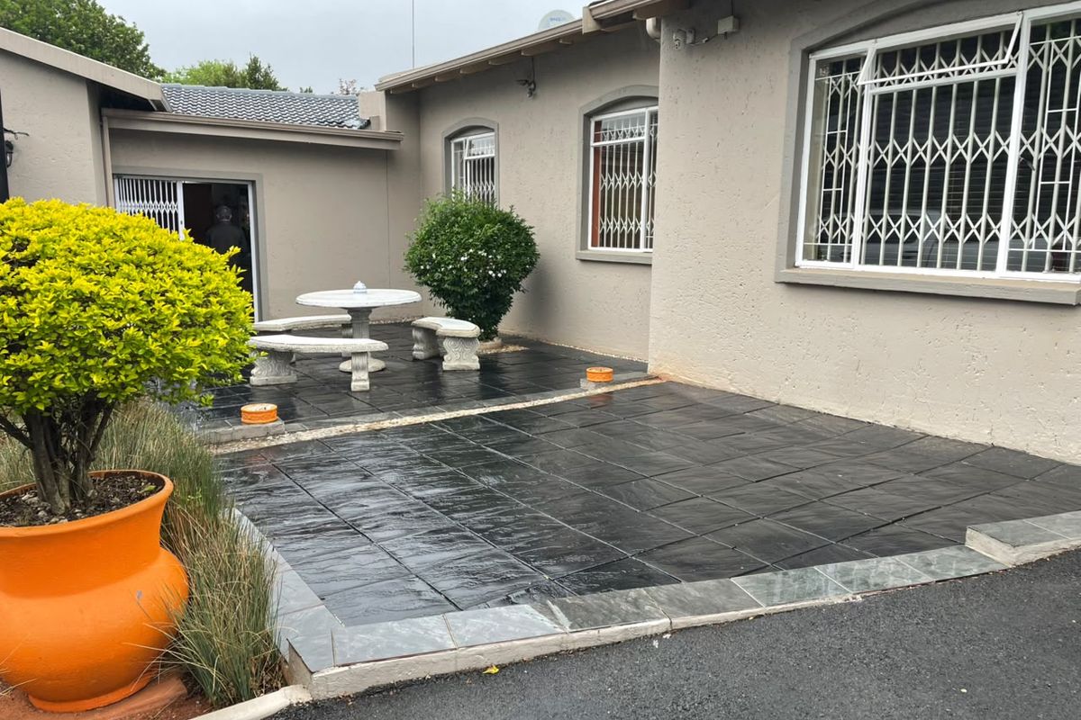 A paved rear patio area featuring dark tiles, security gates on windows, and a sliding door entrance to the home.