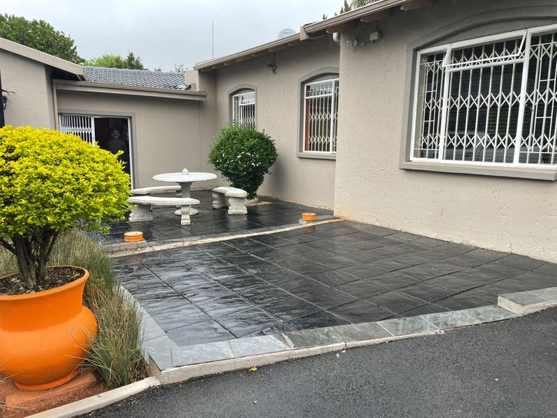 A paved rear patio area featuring dark tiles, security gates on windows, and a sliding door entrance to the home.