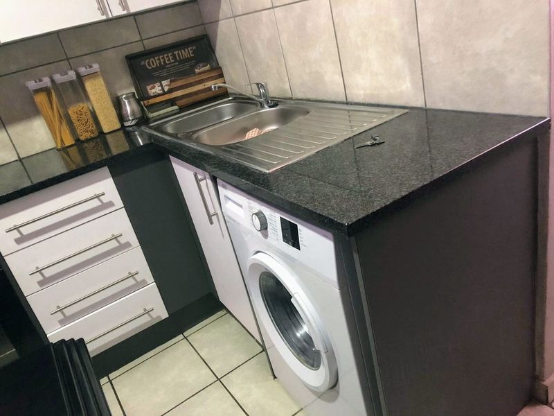 A functional laundry area featuring a stainless steel sink, granite countertops, built-in cabinetry, and an integrated washing machine with tiled finishes.