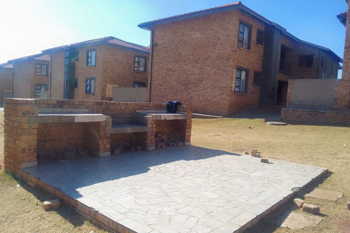 Outdoor communal area featuring a built-in brick braai and paved patio space set against a facebrick apartment complex.