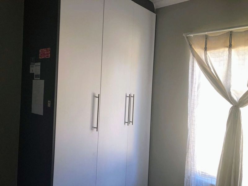 A bedroom featuring a built-in wardrobe with modern handles and a window allowing natural light.