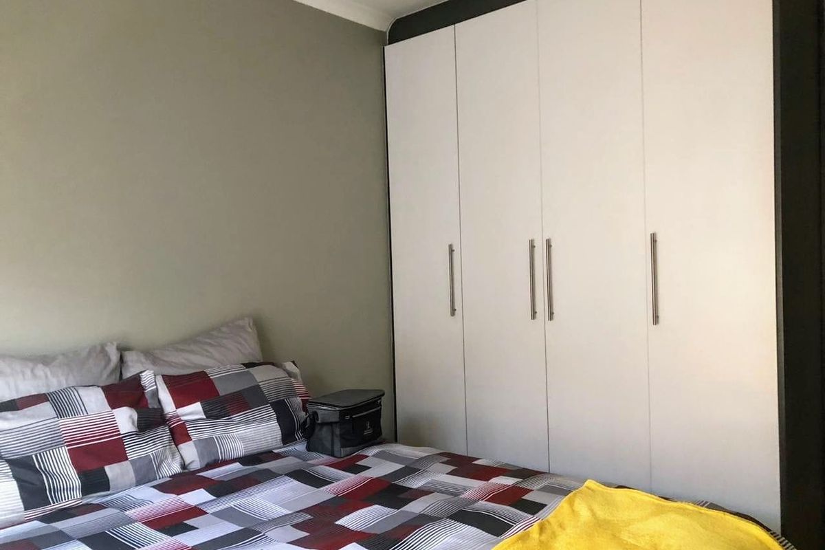 A well-maintained bedroom featuring a large, modern white built-in wardrobe with sleek metal handles and neutral wall finishes.