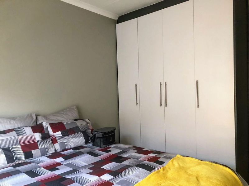 A well-maintained bedroom featuring a large, modern white built-in wardrobe with sleek metal handles and neutral wall finishes.