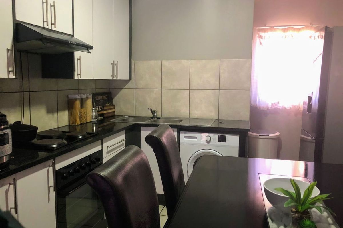 A functional kitchen featuring white cabinetry, dark countertops, a built-in oven with hob, and an integrated washing machine.