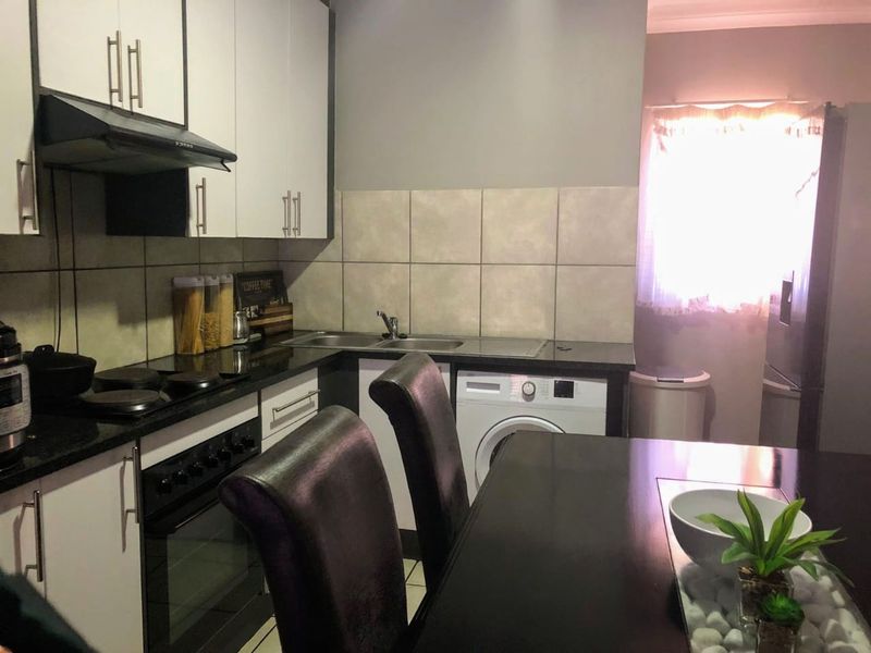 A functional kitchen featuring white cabinetry, dark countertops, a built-in oven with hob, and an integrated washing machine.