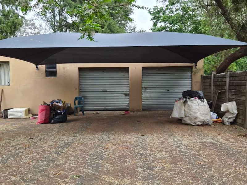 Exterior view of a double garage featuring roller doors, a shade sail structure, and a paved driveway area.