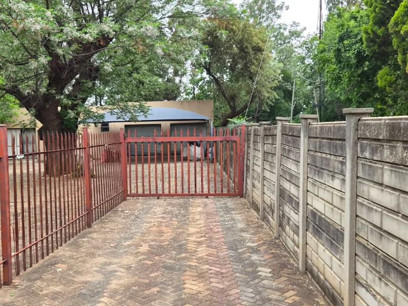 Front exterior view featuring a paved driveway, metal security gate, perimeter fencing, and a double garage.