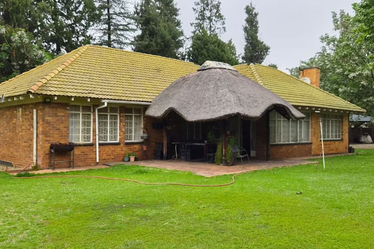Rear view of a brick house featuring a tiled roof, a thatched lapa over a paved patio, and a spacious garden.