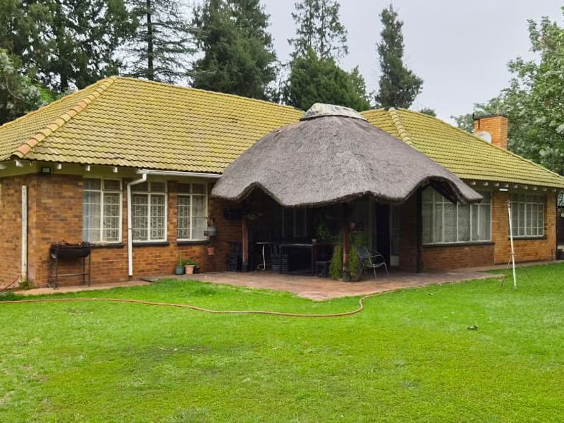 Rear view of a brick house featuring a tiled roof, a thatched lapa over a paved patio, and a spacious garden.