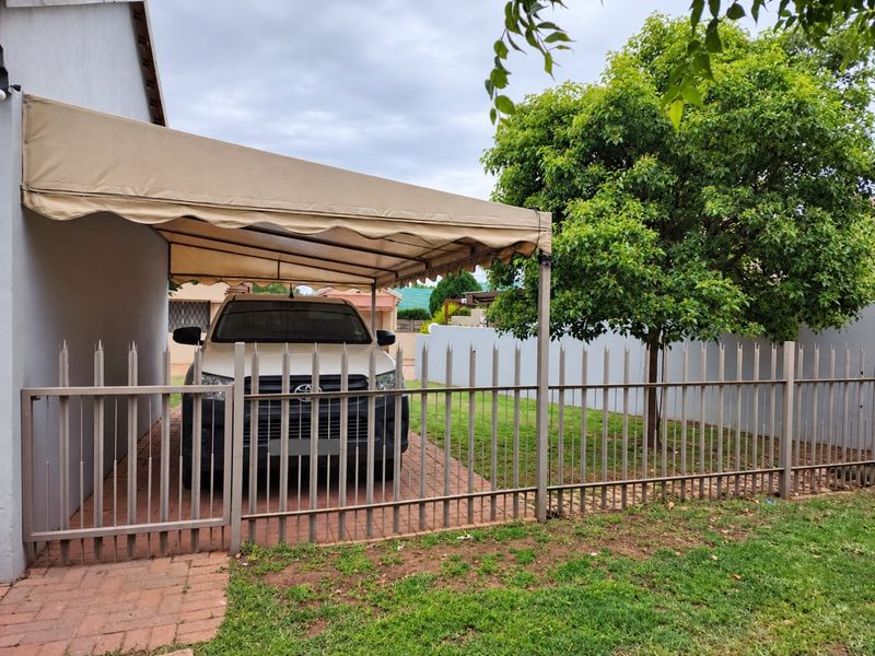 Front exterior view of the townhouse featuring a covered carport, paved driveway, and secure steel palisade fencing.
