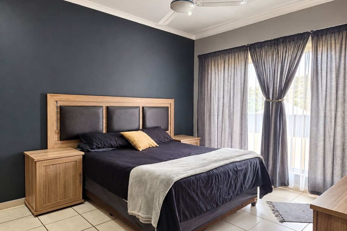 A well-maintained bedroom featuring a dark accent wall, tiled flooring, a ceiling fan, and large sliding glass doors with curtains providing natural light.