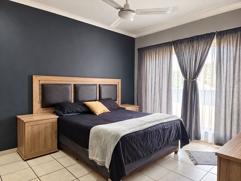 A well-maintained bedroom featuring a dark accent wall, tiled flooring, a ceiling fan, and large sliding glass doors with curtains providing natural light.