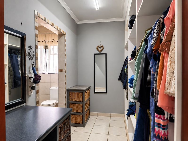 A walk-in dressing room featuring built-in shelving and cabinetry, with tiled flooring and direct access to an adjoining bathroom.
