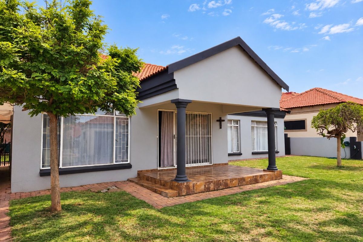 A well-maintained townhouse exterior featuring a covered patio with decorative columns, terracotta roof tiles, and a neat garden area.