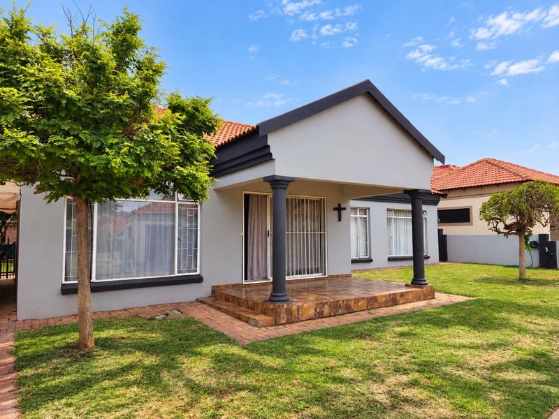 A well-maintained townhouse exterior featuring a covered patio with decorative columns, terracotta roof tiles, and a neat garden area.