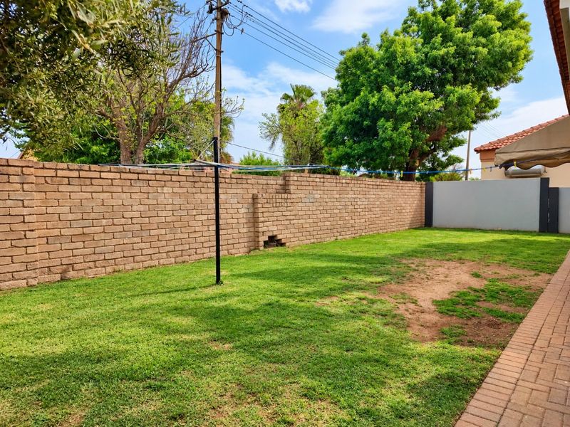 A private rear garden featuring a lawn area, paved walkway, and a brick boundary wall with a rotary clothesline.
