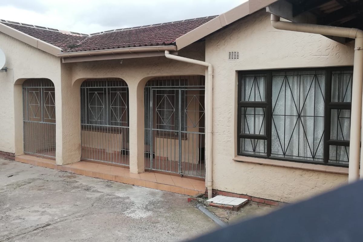 Rear exterior view of the house featuring a tiled roof, security gates on the patio area, and a concrete driveway.