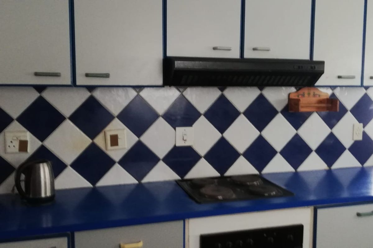 A functional kitchen featuring built-in cabinetry, a blue laminate countertop, an electric hob, and a classic blue and white diamond-patterned tiled backsplash.