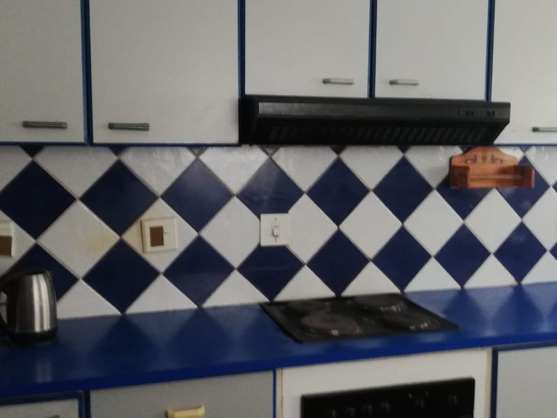 A functional kitchen featuring built-in cabinetry, a blue laminate countertop, an electric hob, and a classic blue and white diamond-patterned tiled backsplash.
